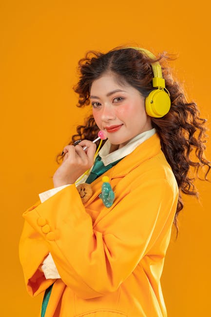 Confident woman posing with headphones and lollipop against vibrant orange backdrop.